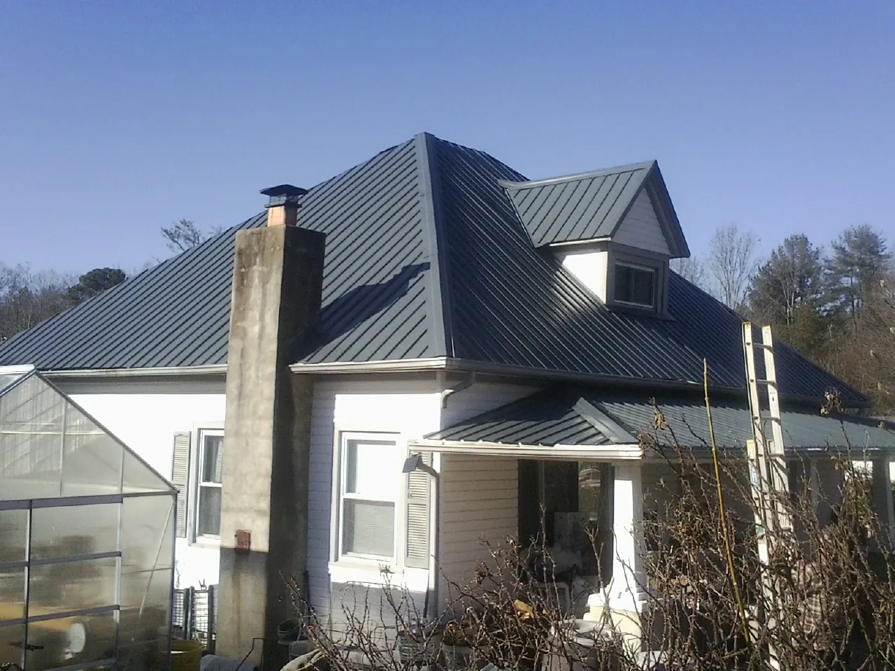 Dark blue standing seam metal roof on a white farmhouse with dormer — Slate & Tile Roof Repair by Roofing Brothers in Gaylord
