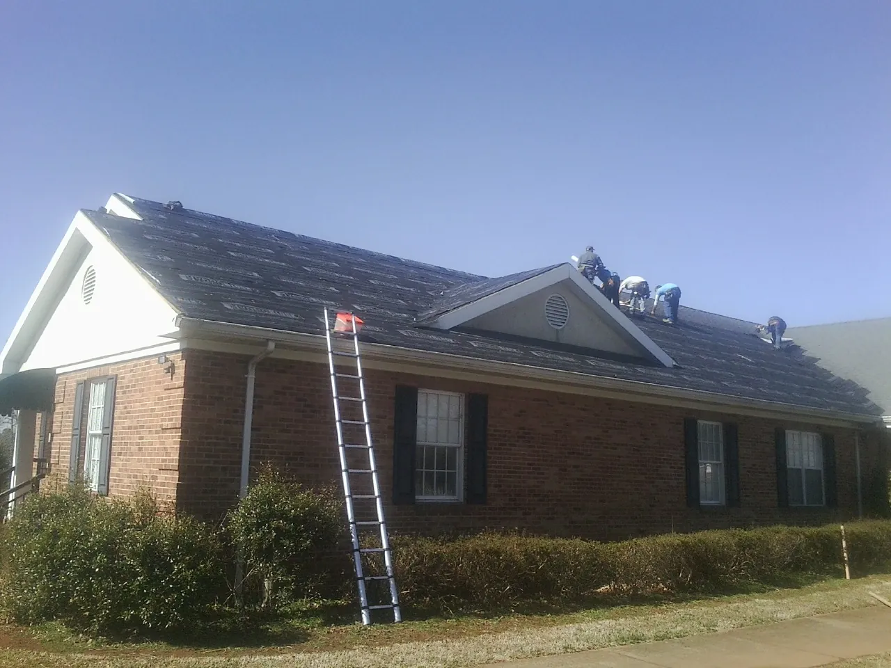 Crew tearing shingles off a brick ranch roof with a ladder set — Emergency Roof Repair work by our crew in Gaylord