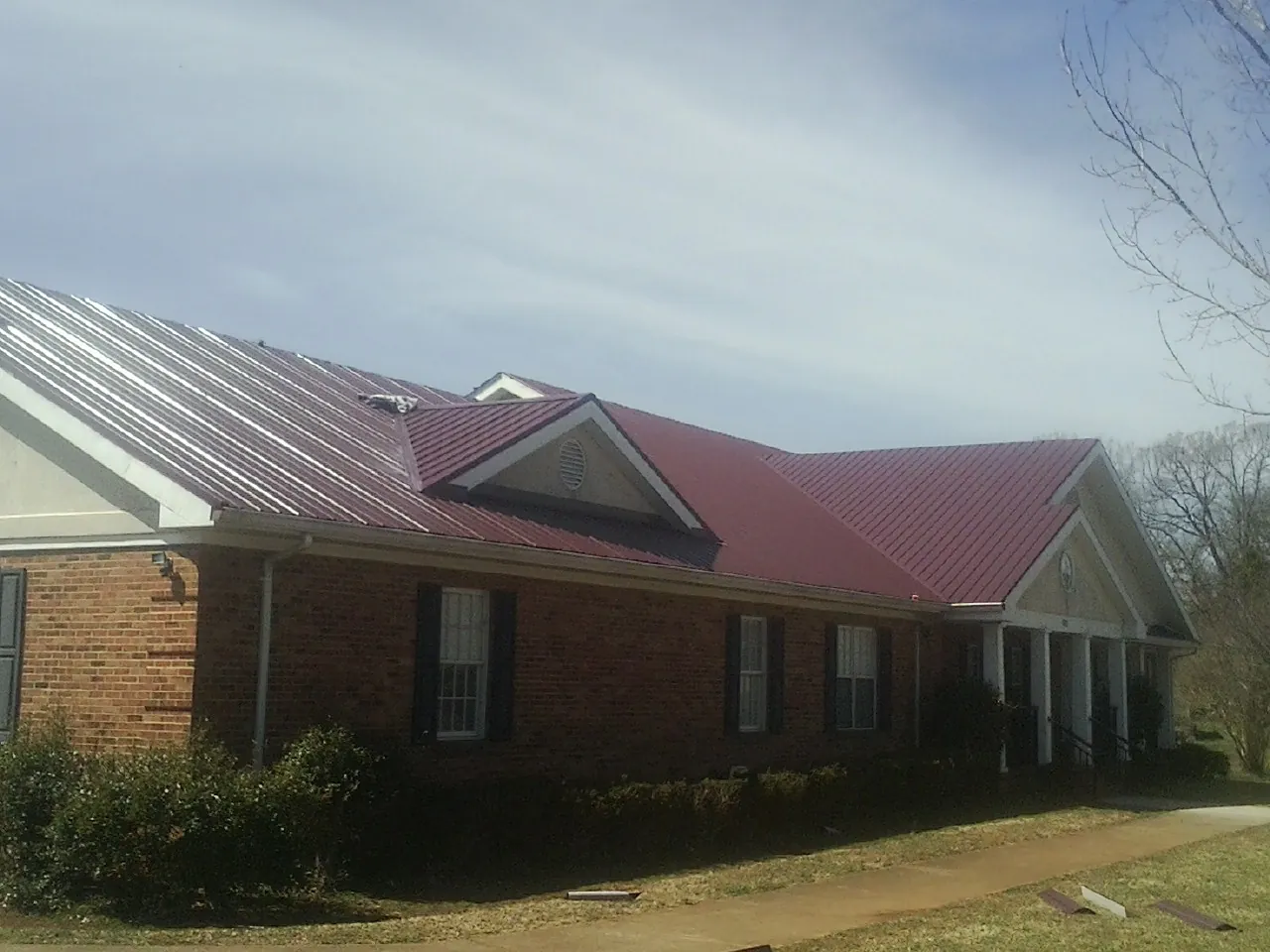 Red metal roof with gabled entries on a long brick building, from a Hail Damage Roof Repair job in Gaylord
