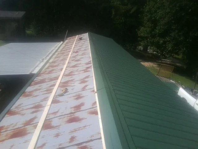 Old rusted panels beside newly installed green metal roofing — Wind Damage Roof Repair by Roofing Brothers in Gaylord