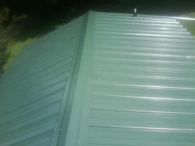 New green metal panels meeting at the ridge of a roof — Flat Roof Repair work by our crew in Gaylord