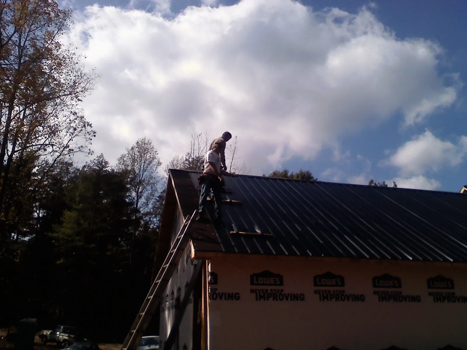 Roofer fastening dark metal panels high against a cloudy sky, from a Roof Inspection job in Gaylord