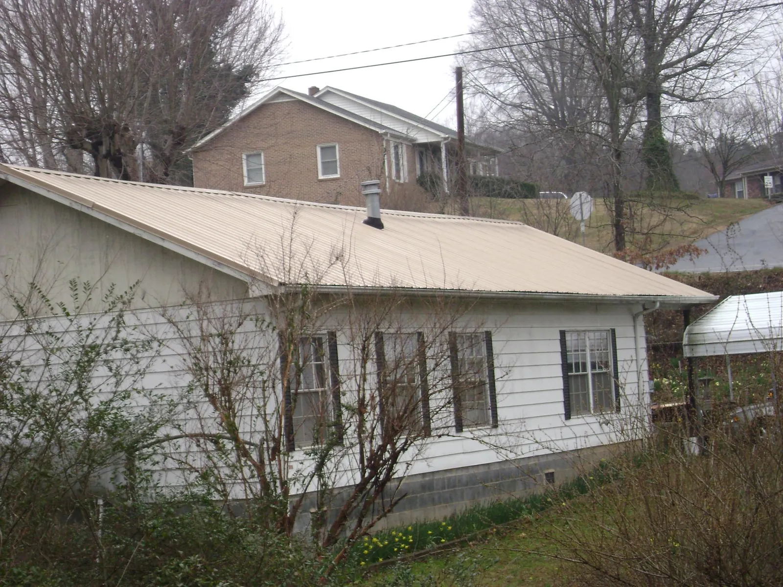 Tan metal roof on a white sided house set into a hillside — Commercial Roofing by Roofing Brothers in Gaylord